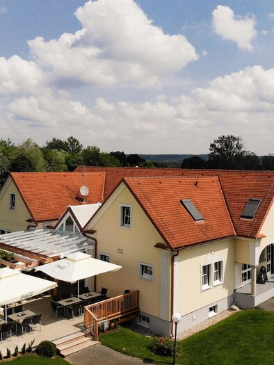 Ein hübsches Gebäude mit rotem Dach und grünem Garten. Vor dem Haus befinden sich Außenterrassen mit Sonnenschirmen. | © Das Puchis