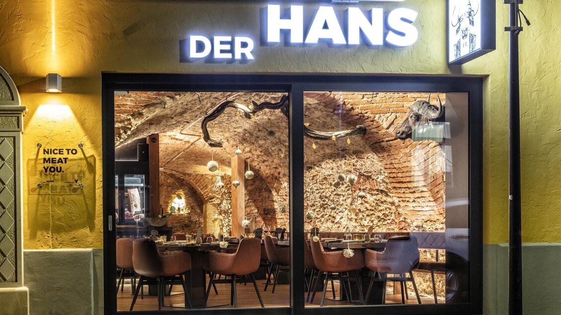 Ein gemütliches Restaurant mit einem einladenden Ambiente. Die Fenster zeigen eine stilvolle Inneneinrichtung mit Holzelementen. | © Photoworkers