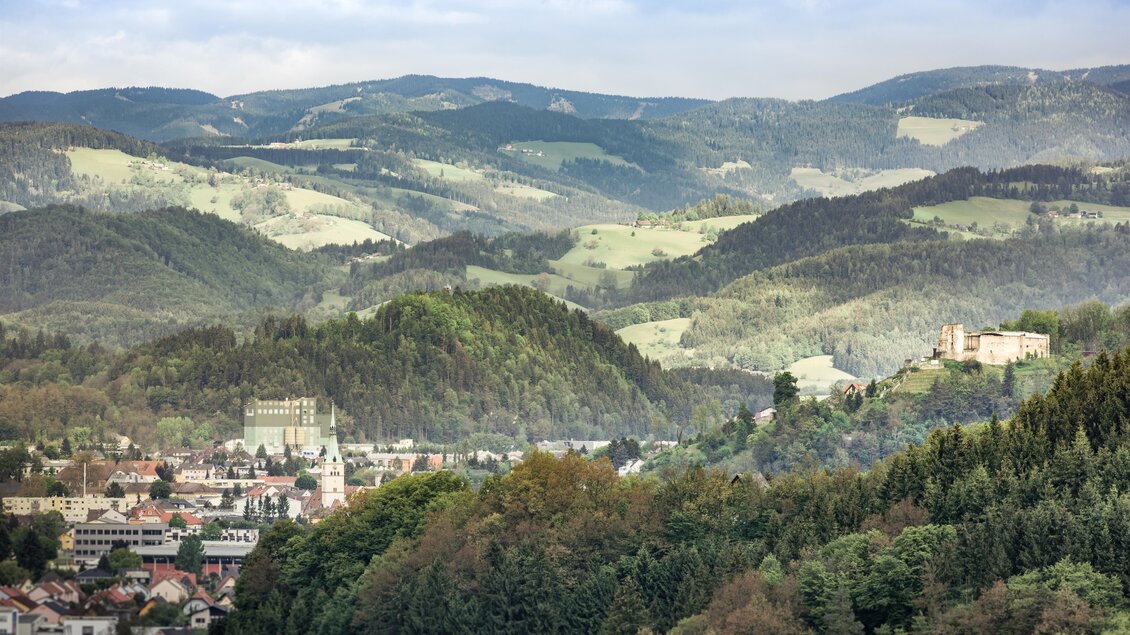 Panoramablick über Voitsberg mit bewaldeten Hügeln und der Burgruine Obervoitsberg auf dem Schlossberg im Hintergrund | © TV Region Graz - Die Abbilerei