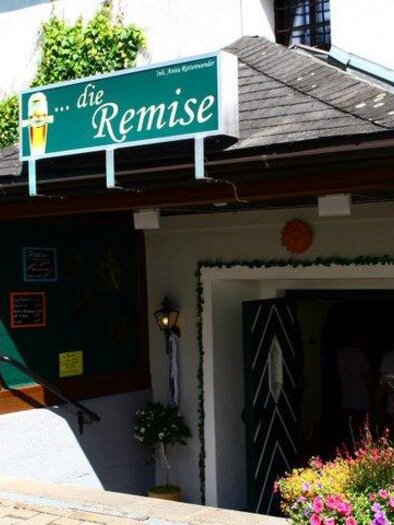 An inviting entrance to a restaurant called "die Remise". The area is decorated with colorful flowers and a sign. | © Die Remise