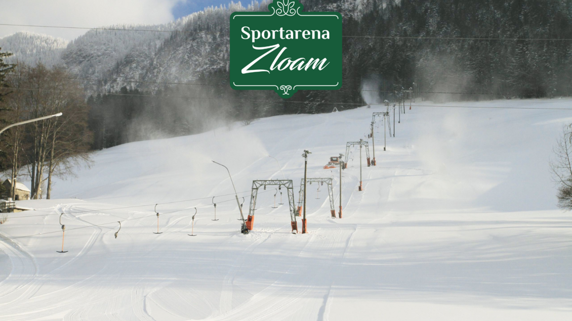 Eine schneebedeckte Piste mit Skiliften im Hintergrund. Die Landschaft ist von Bergen umgeben und zeigt einen klaren Wintertag. | © www.zloam.at