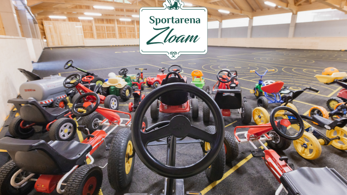 Eine Sammlung von bunten Spielzeugfahrzeugen in einer großen Halle. Im Hintergrund sind Markierungen auf dem Boden sichtbar, die eine Rennstrecke darstellen. | © www.zloam.at