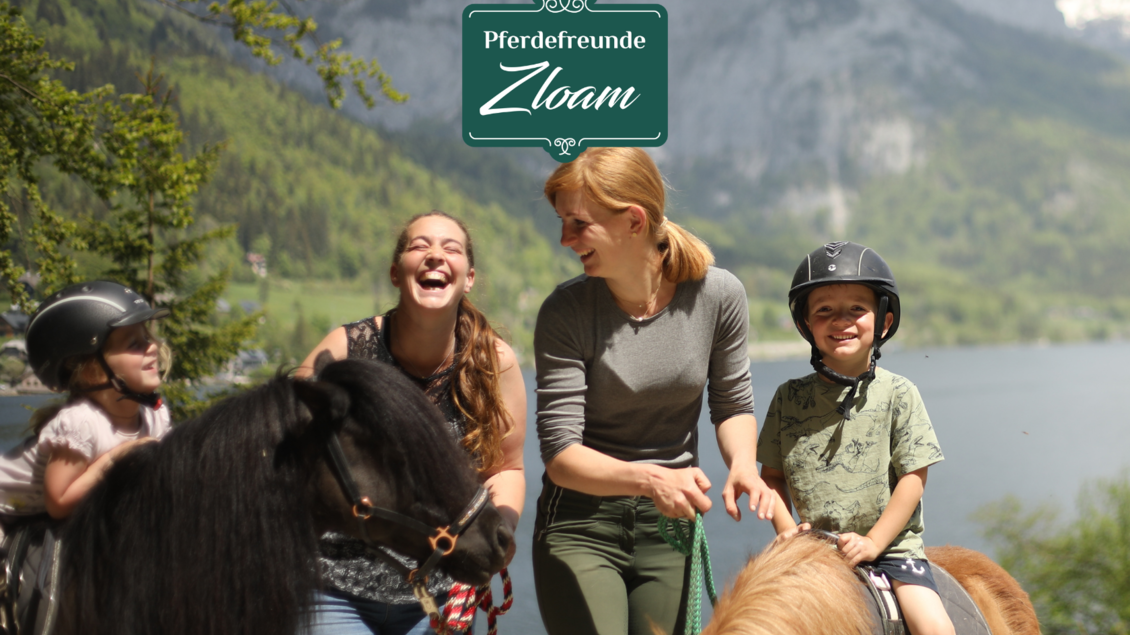 Eine fröhliche Gruppe von Menschen reitet auf Ponys an einem malerischen See. Im Hintergrund sind Berge und eine grüne Landschaft zu sehen. | © www.zloam.at