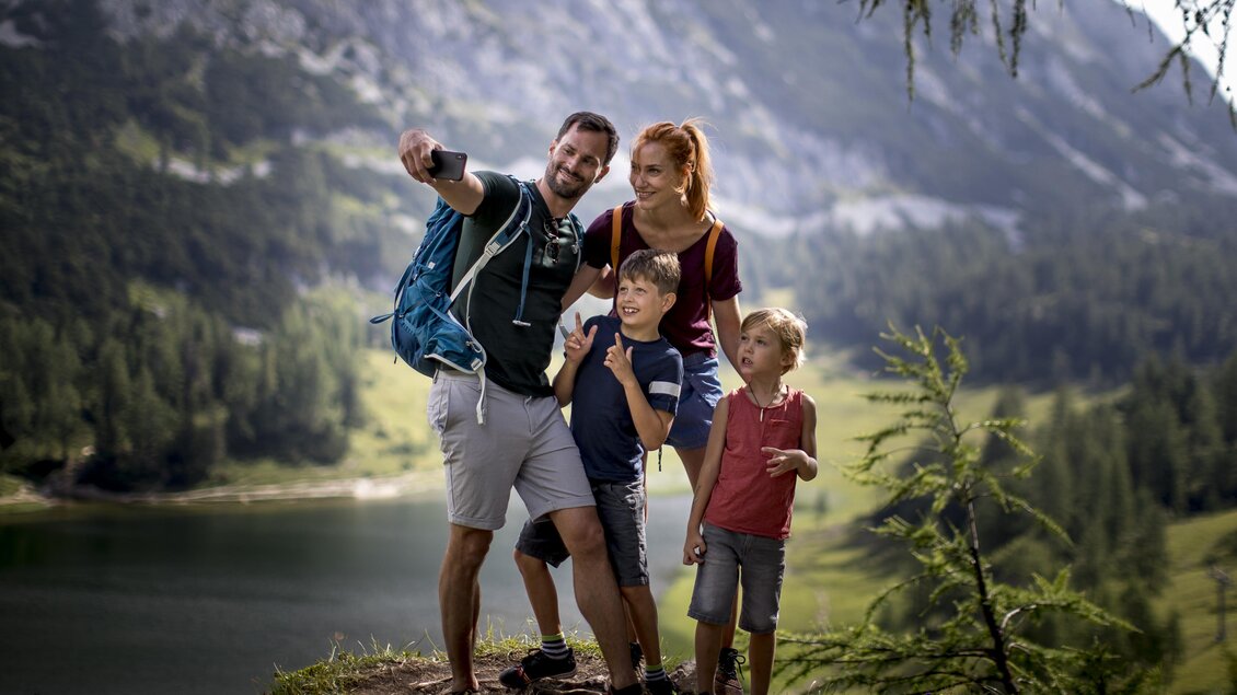 <p>Eine Familie macht nach einer erfolgreichen Wanderung zum Großsee ein Selfie vor dem See auf der Tauplitz. Im Hintergrund sind die Berge des Ausseerlandes und viel grüne Natur zu sehen.</p> | © Die Tauplitz/Tom Lamm