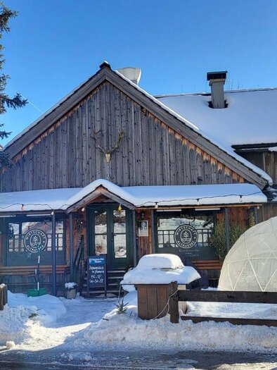 A charming wooden house in the snow with a round glass cage beside it. The sky is clear and blue, creating a cozy atmosphere. | © Petra Kirchschlager