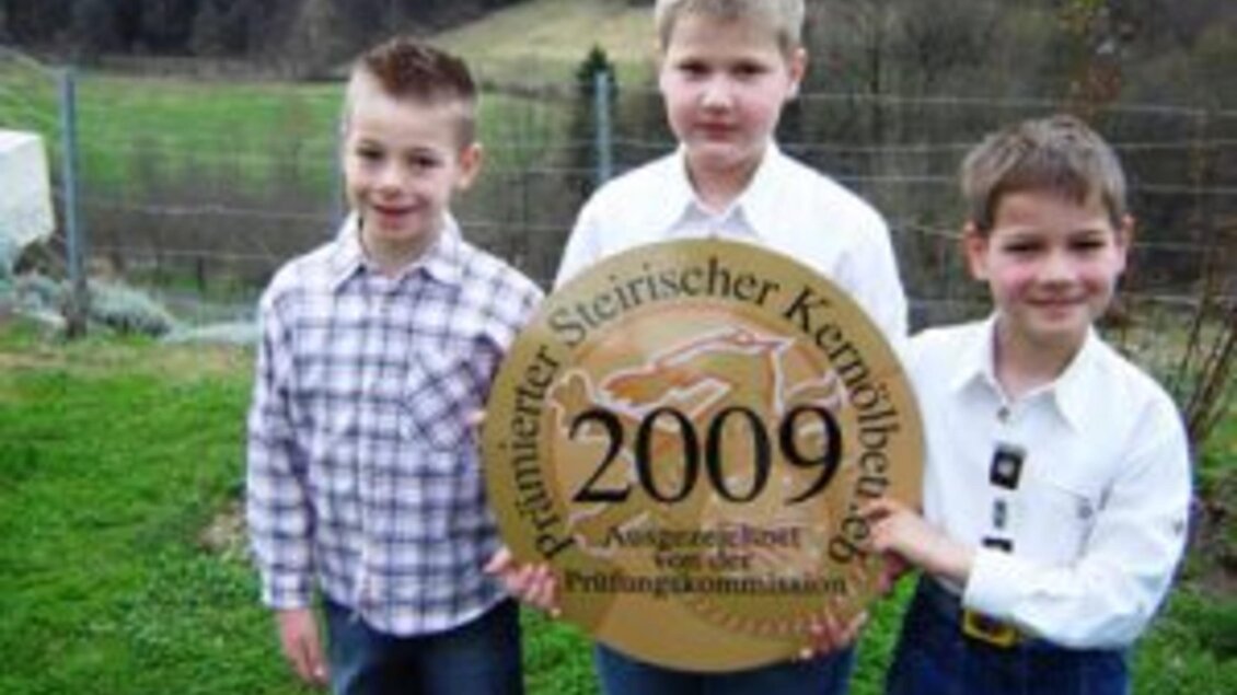 Drei Jungen stehen auf einer Wiese und halten ein großes Schild mit der Aufschrift "2009". Sie sind in eleganter Kleidung gekleidet und lächeln in die Kamera. | © Gästehaus Klampfer