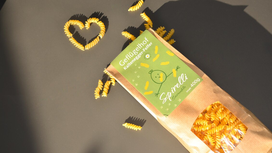 Eine packung mit Spiralnudeln aus Vollkorn steht auf einem Tisch. Um die Packung liegen verschiedene Nudeln in Form eines Herzens. | © Kaltenegger
