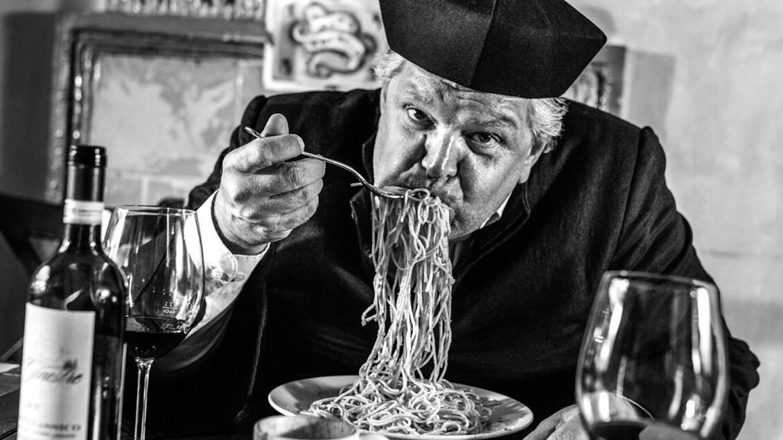 Ein Mann trägt eine traditionelle Kopfbedeckung und genießt eine große Portion Spaghetti. Auf dem Tisch stehen Weingläser und eine Tasse Kaffee. | © Toni Muhr