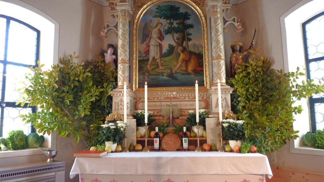 Ein festlich geschmückter Altar mit Pflanzen, Kerzen und einer kunstvollen Darstellung. Im Hintergrund sind Fenster, die natürliches Licht hereinlassen. | © Mares Rastl
