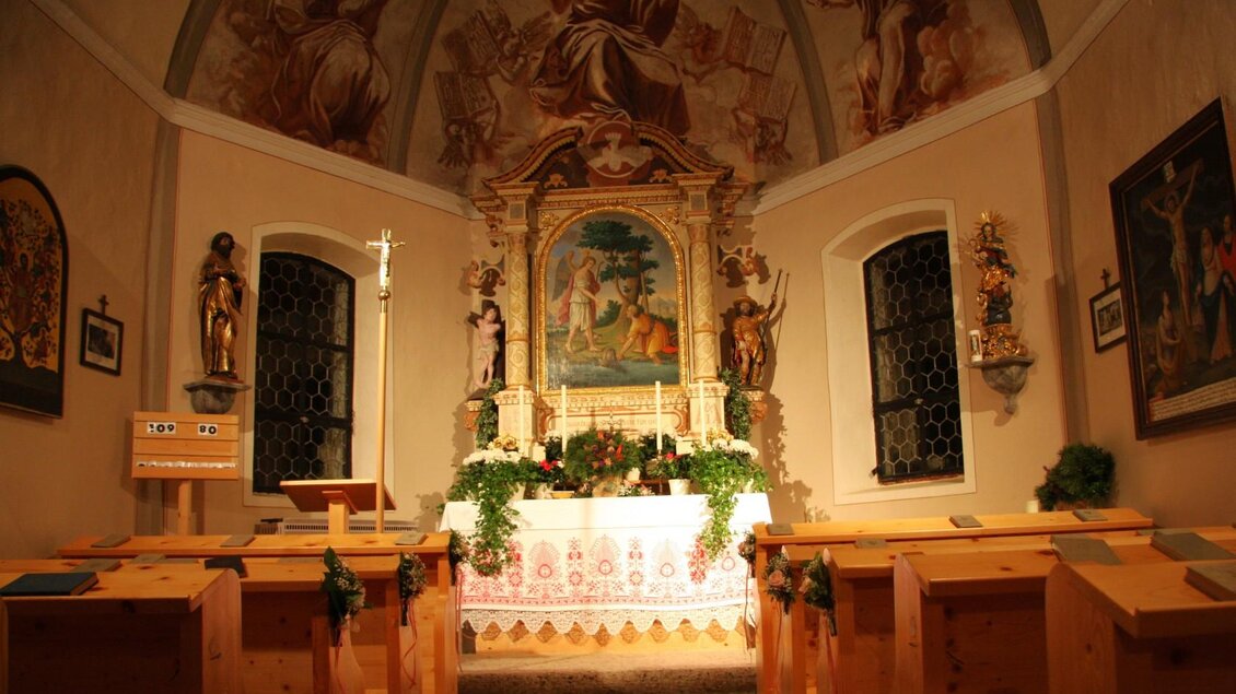 Eine kleine, dekorierte Kapelle mit einem Altartisch und bunten Wandmalereien. Holzbankreihen sind um den Altar herum angeordnet. | © Mares Rastl