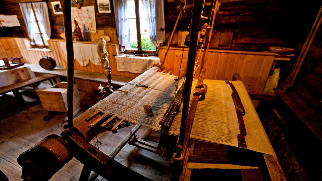 Ein historischer Webstuhl in einer gemütlichen Holzhütte. Der Raum ist rustikal eingerichtet mit Fenstern, die natürliches Licht hereinlassen. | © Holzwelt Murau