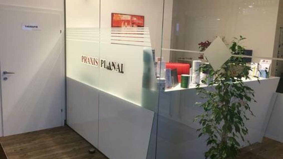 Ein moderner Empfangsbereich einer Praxis mit einer Glasscheibe. Im Hintergrund sind Beratungstische und Pflanzen zu sehen. | © Klaus Karrer