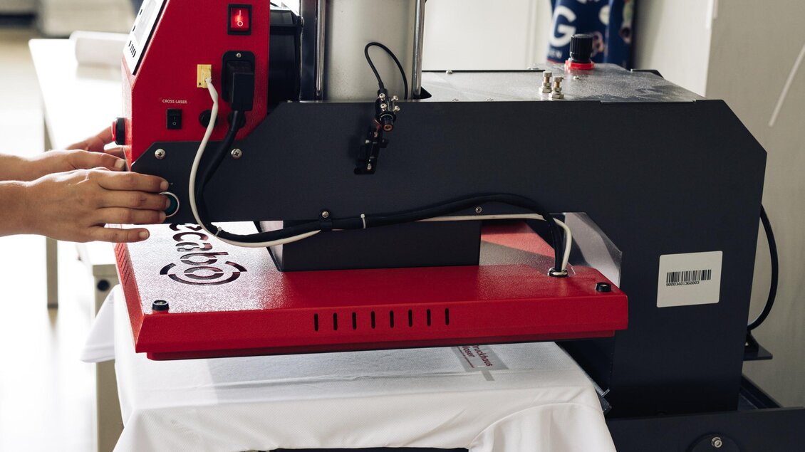 Textildruckmaschine beim Bedrucken eines weißen Shirts mit dem Logo von Druckhaus Moser. | © Bernd Grosseck