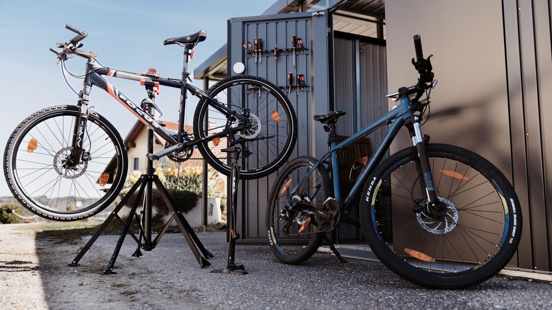 Zwei Mountainbikes stehen an einer Werkstatt. Im Hintergrund ist eine offene Tür zu sehen. | © Martinhof