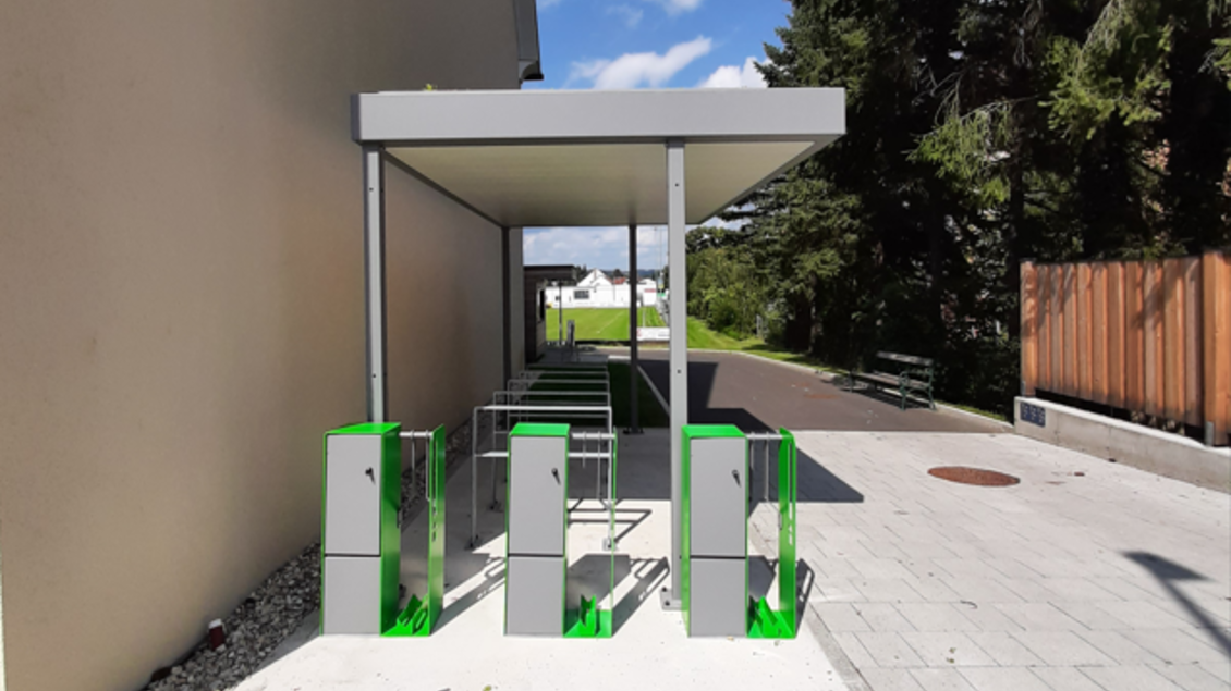 Eine moderne Fahrradstation mit mehreren Abstellplätzen unter einem Vordach. Im Hintergrund sind Bäume und ein Gehweg sichtbar. | © Stadtgemeinde Fehring