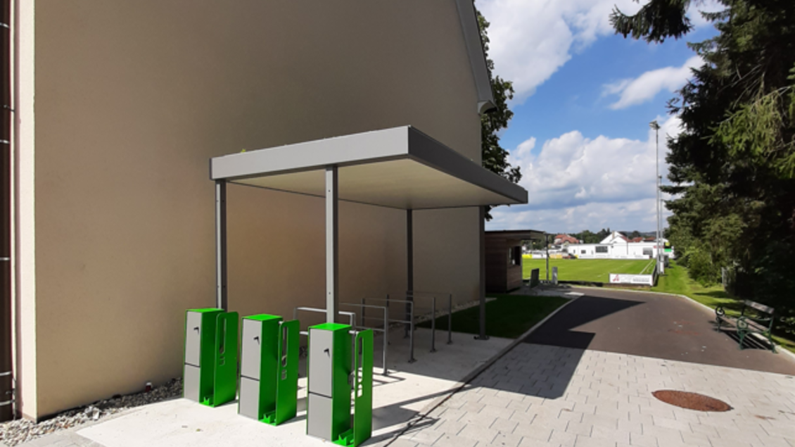 Ein moderner Zugang mit grünen Automaten steht an einer Wand. Im Hintergrund sind ein asphaltiertes Weg und Bäume sichtbar. | © Stadtgemeinde Fehring