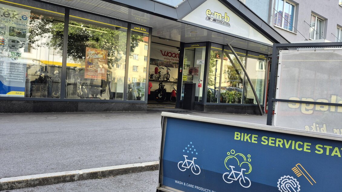 Ein Geschäft mit einer großen Glasfront und Fahrradzubehör. Im Vordergrund befindet sich ein Schild für einen Fahrradservice. | © Andrea Stelzer