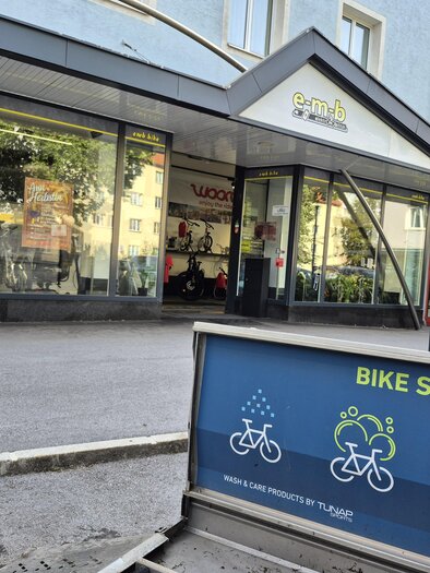 Ein Geschäft mit einer großen Glasfront und Fahrradzubehör. Im Vordergrund befindet sich ein Schild für einen Fahrradservice. | © Andrea Stelzer