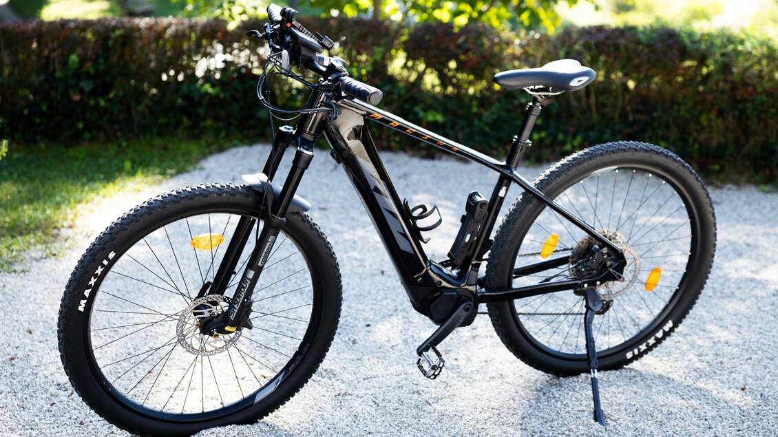 Ein schwarzes Mountainbike steht auf einem Kiesweg. Im Hintergrund sind grüne Pflanzen und Bäume zu sehen. | © Kerstin Godl