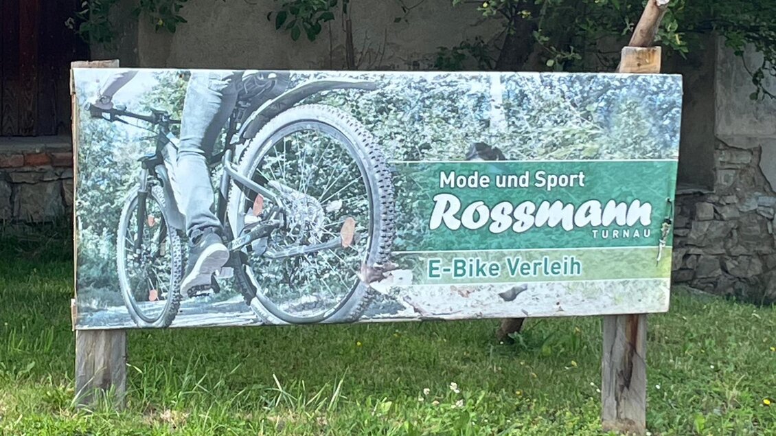 Ein Werbeschild für einen E-Bike-Verleih. Es zeigt das Rad eines E-Bikes und informiert über Mode und Sport. | © Doris Westphal