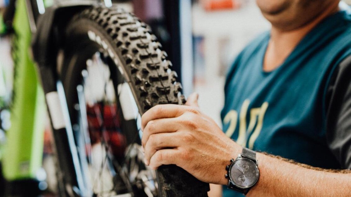 Ein lächelnder Mann repariert ein Mountainbike in einem Fahrradgeschäft. Er untersucht das Rad und arbeitet an der Wartung.