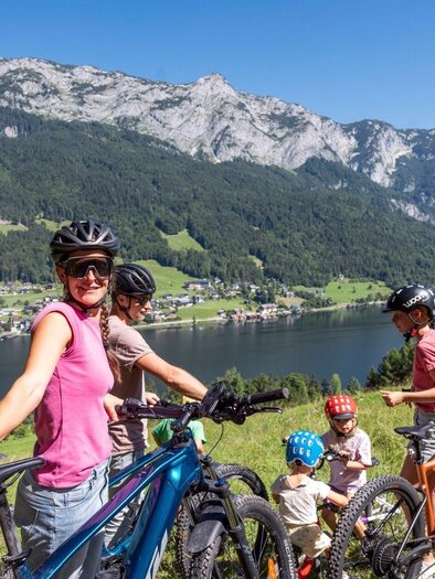 Eine Familie macht eine Fahrradtour in den Bergen. Im Hintergrund sieht man einen klaren See und eine beeindruckende Berglandschaft. | © www.zloam.at