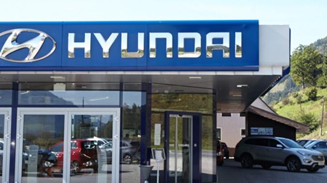 Ein modernes Hyundai-Autohaus mit großen Fenstern und einem klaren Logo. Mehrere Autos stehen auf dem Parkplatz in einer grünen Umgebung. | © auto-schnitzer.at