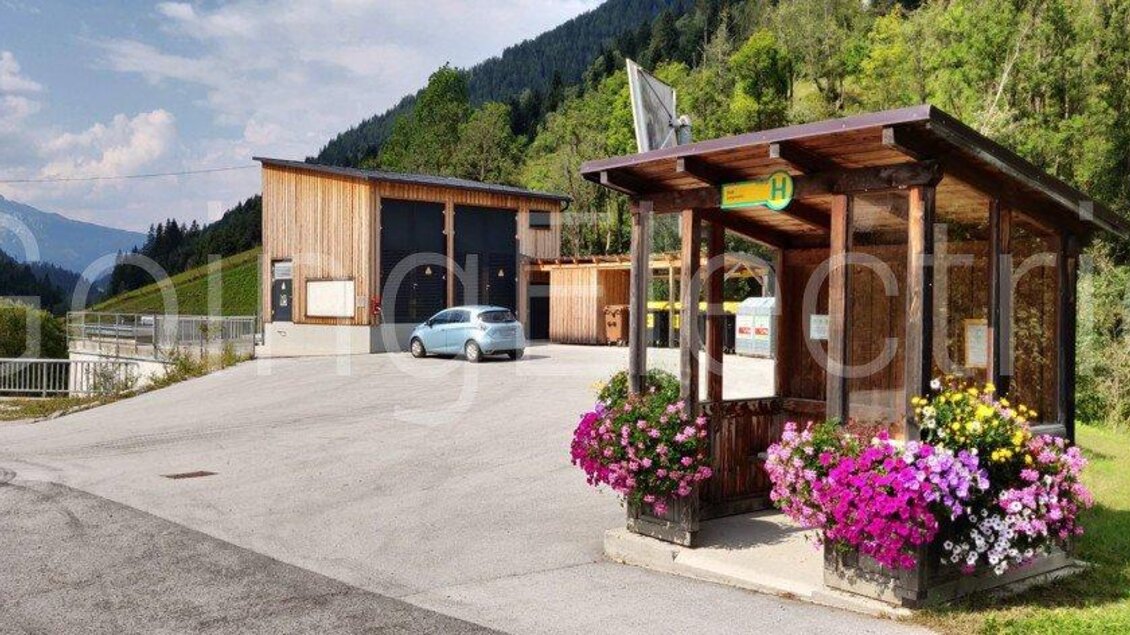 Ein kleiner Parkplatz mit einem Holzgebäude und einer Infostelle. Bunte Blumenbeete schmücken die Umgebung. | © Going Electric