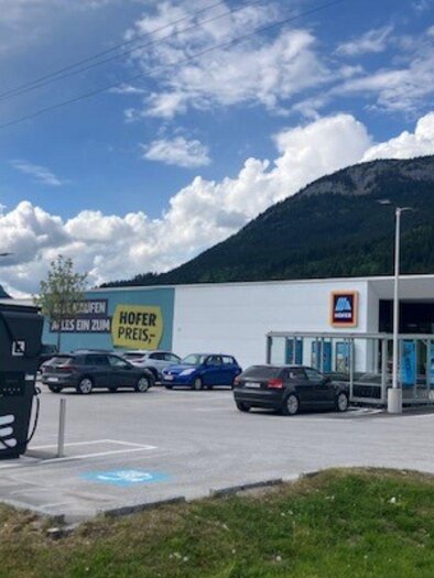 Two charging stations for electric cars are located in a large parking lot. In the background, there is a large building, the Hofer supermarket. | © TVB Ausseerland Salzkammergut (c) Heike Temmel