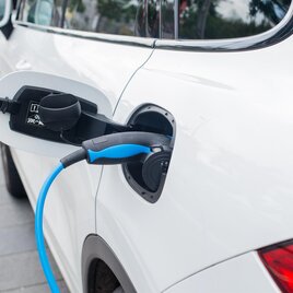 Ein weißes Elektroauto lädt an einer Ladestation. Das Ladekabel ist an die Fahrzeugseite angeschlossen. | © AdobeStock_189648321