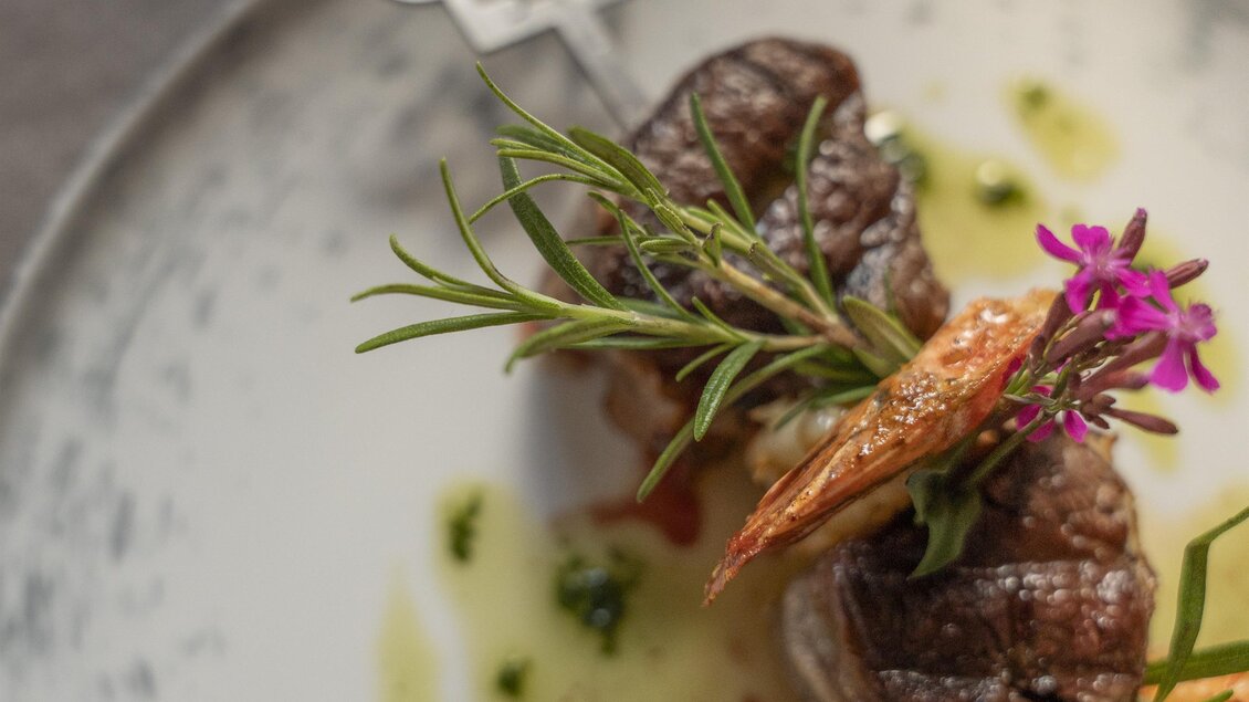 Ein kunstvoll angerichteter Teller mit gegrilltem Fleisch und Garnelen. Frische Kräuter und essbare Blüten verleihen dem Gericht eine elegante Note.