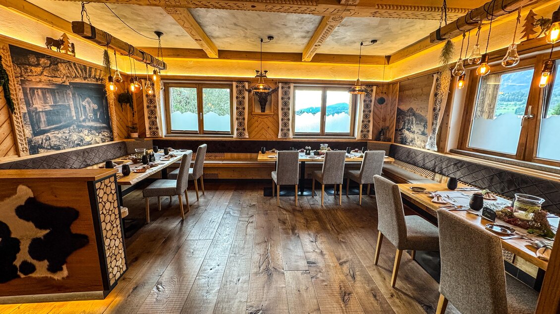 Ein gemütlicher Restaurantbereich mit Holzmöbeln und warmem Licht. Große Fenster bieten einen Blick auf die Landschaft.