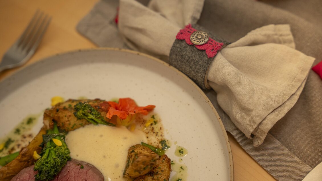 Ein schöner Teller mit zartem Fleisch, Gemüse und Püree. Neben dem Teller liegen dekorative Stoffservietten.