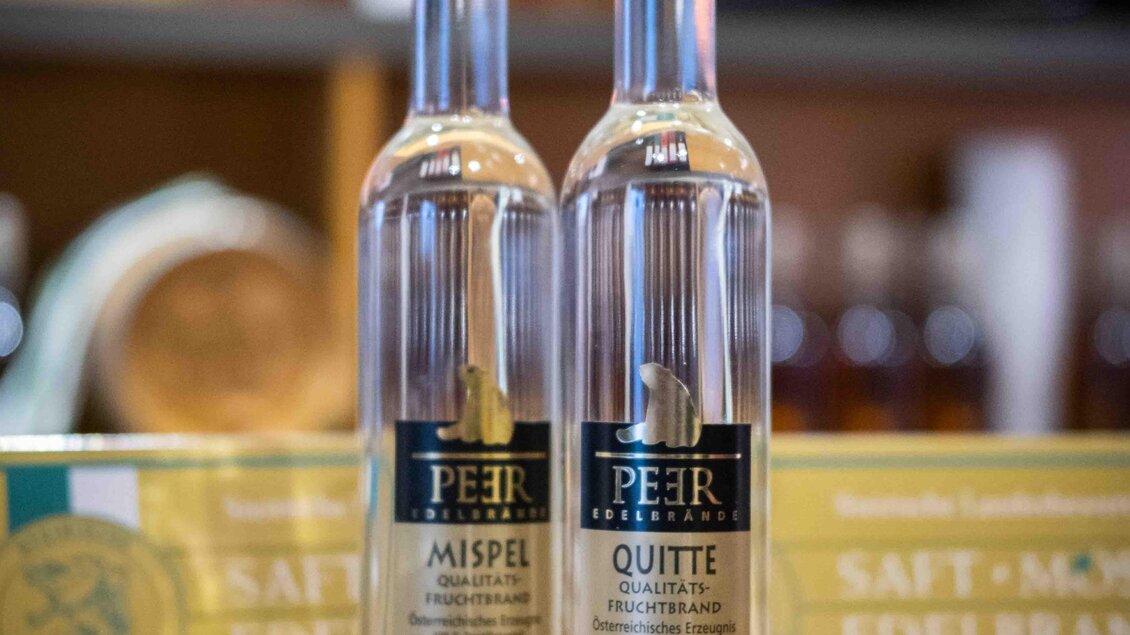 Zwei Flaschen klarer Schnaps stehen auf einem Holztisch. Daneben befindet sich eine Auszeichnung für hochwertigen Saft. | © Edelbrand Peer