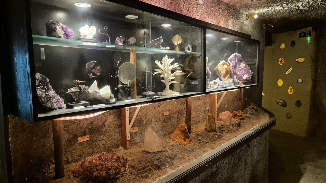 Ein dekoratives Vitrinengestell zeigt verschiedene Mineralien und Kristalle. Im Hintergrund sind die Wände grob und beleuchtet, was eine mystische Atmosphäre schafft. | © TVB Murau
