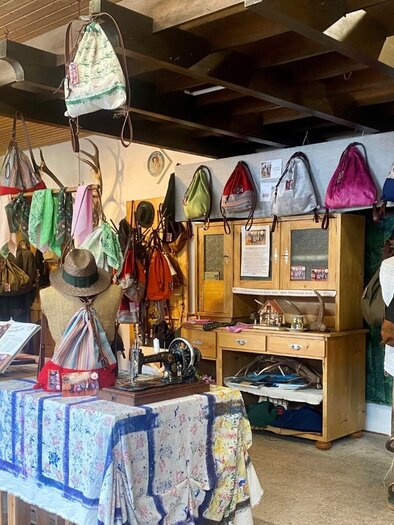 A creative shop with many bags hanging on the wall. In the foreground, there is a table with various accessories and fabrics. | © TVB Ausseerland/Bettina Scheck