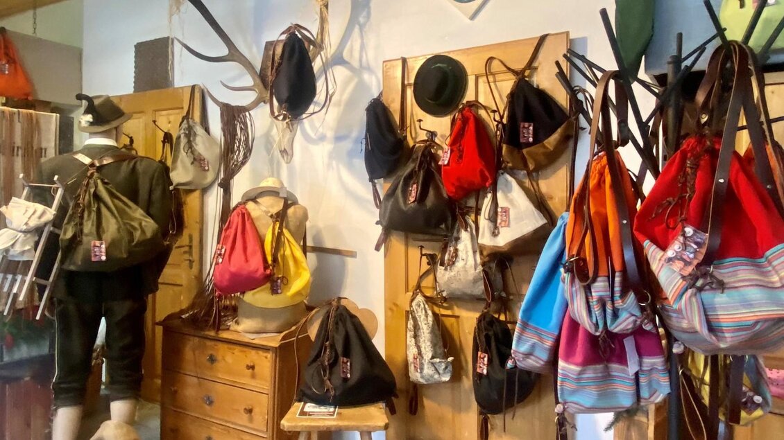 Ein Raum mit verschiedenen Taschen aus Leder und Stoff, die an Wänden aufgehängt sind. Im Vordergrund steht eine Figur mit einer Tasche, während ein Holztisch im Hintergrund sichtbar ist. | © TVB Ausseerland/Bettina Scheck