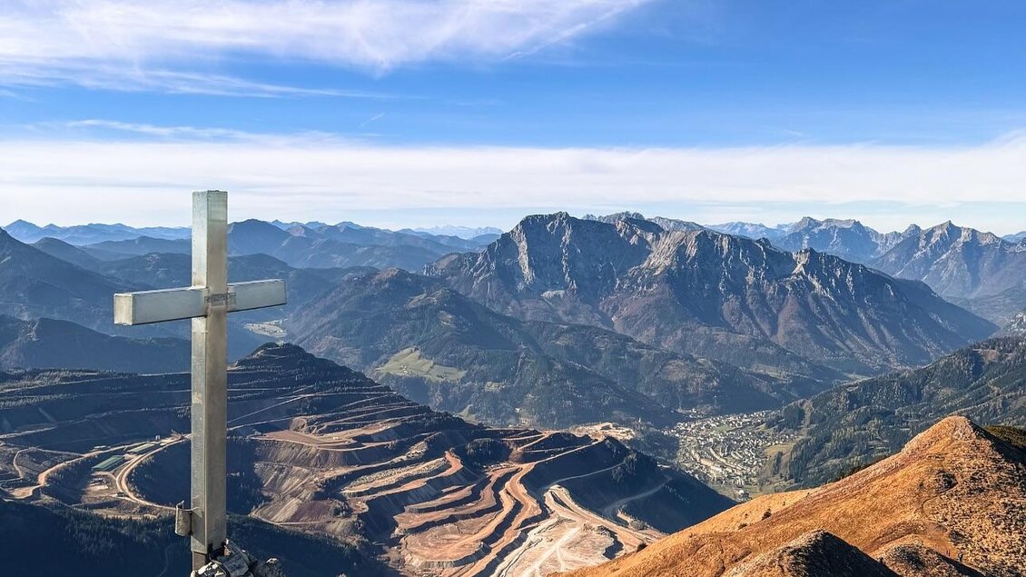 Ein Kreuz auf einem Felsen mit Blick auf eine beeindruckende Berglandschaft. Im Hintergrund sind hohe Berge und ein klarer Himmel zu sehen. | © Simona Stanciu