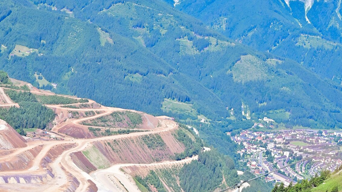 Ein malerischer Bergblick mit einem großen Gebirgszug im Hintergrund. Im Vordergrund sind Seilbahnen, die über eine grüne Wiese fahren. | © Viktoria Hirtler