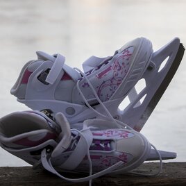 Zwei Schlittschuhe auf Holzbank vor gefrorener Eisfläche in Graz.  | © TV Region Graz - Jimmy Lunghammer
