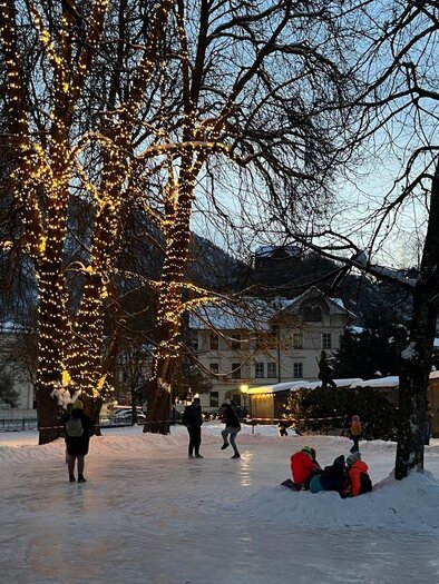 Eine winterliche Szene mit schneebedeckten Bäumen und einem festlich beleuchteten Platz. Menschen genießen die winterliche Atmosphäre und die schöne Umgebung. | © TVB Ausseerland Salzkammergut/Gabi Grill