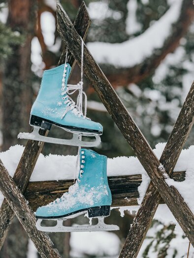 Eislaufschuhe in helblau hängen an einem Holzgestell. Der Schnee um sie herum schafft eine winterliche Atmosphäre. | © Lupi Spuma