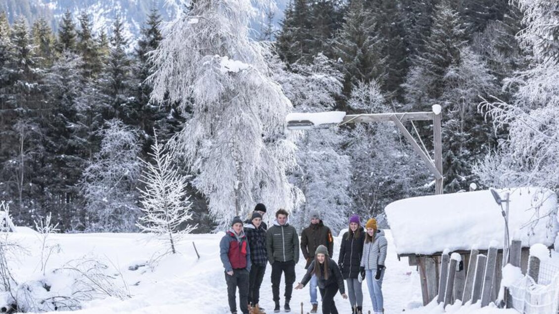 Eine Gruppe von Menschen steht auf einer gefrorenen Oberfläche in einer winterlichen Landschaft. Im Hintergrund sind schneebedeckte Berge und Bäume zu sehen. | © Waldhäuslalm/Martin Huber