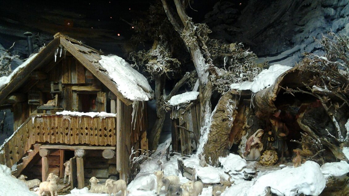 Eine winterliche Szene mit einem Holzhaus und schneebedeckten Bäumen. Im Vordergrund sind Tiere zu sehen, die die verschneite Landschaft erkunden. | © Elisabeth Schupfer