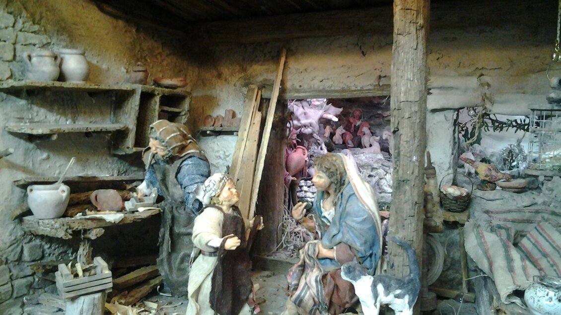 Eine historische Szene mit Figuren in einem rustikalen Raum. Es gibt Regale mit Töpfen und eine Frau, die mit einem Kind und einem Kätzchen interagiert. | © Elisabeth Schupfer