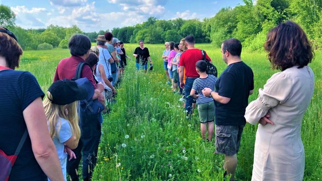 Eine Gruppe von Menschen steht auf einem Feld und hört einem Referenten zu. Der Himmel ist blau mit einigen Wolken, umgeben von grüner Vegetation. | © Martina Schmidt