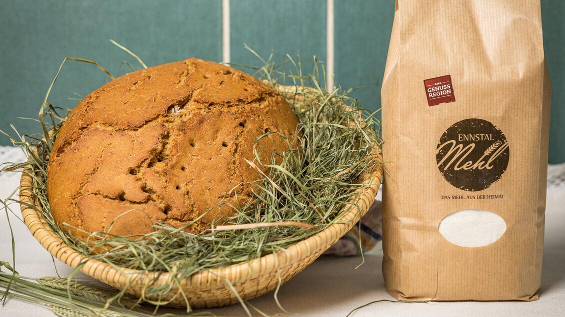 Ein frisch gebackenes Brot in einem Korb, umgeben von Heu. Neben dem Korb steht eine Packung Mehl. | © Netzwerk Kulinarik wildbild