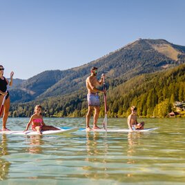 Eine Familie steht auf Stand-Up Paddle-Boards im ruhigen Wasser eines Sees. Im Hintergrund sind Berge und Bäume zu sehen. | © TV Hochsteiermark | Rudy Dellinger