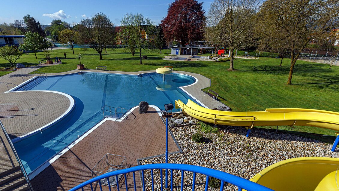 Ein Pool mit einer gelben Rutsche und einer großen Grünfläche rundherum. Die Umgebung ist sonnig und einladend. | © Freibad_Frauental_(c) DI Robert Sackl