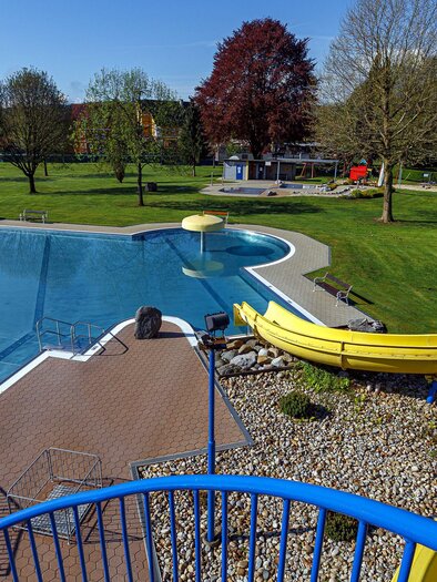 Ein Pool mit einer gelben Rutsche und einer großen Grünfläche rundherum. Die Umgebung ist sonnig und einladend. | © Freibad_Frauental_(c) DI Robert Sackl